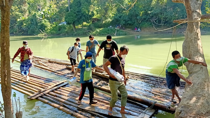 Photo of people holding medical supplies crossing a river on bamboo rafts.
