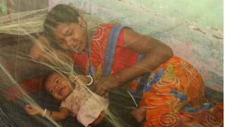 Mother and infant smiling under green bed net. Photo by Ehtisham Husain for the President's Malaria Initiative