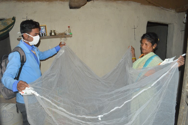 Field worker helping local woman install bednet in Mandla, India. 